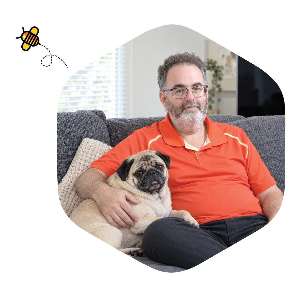 Brad sitting on a grey sofa at home with his pug resting beside him and his arm around the dog.